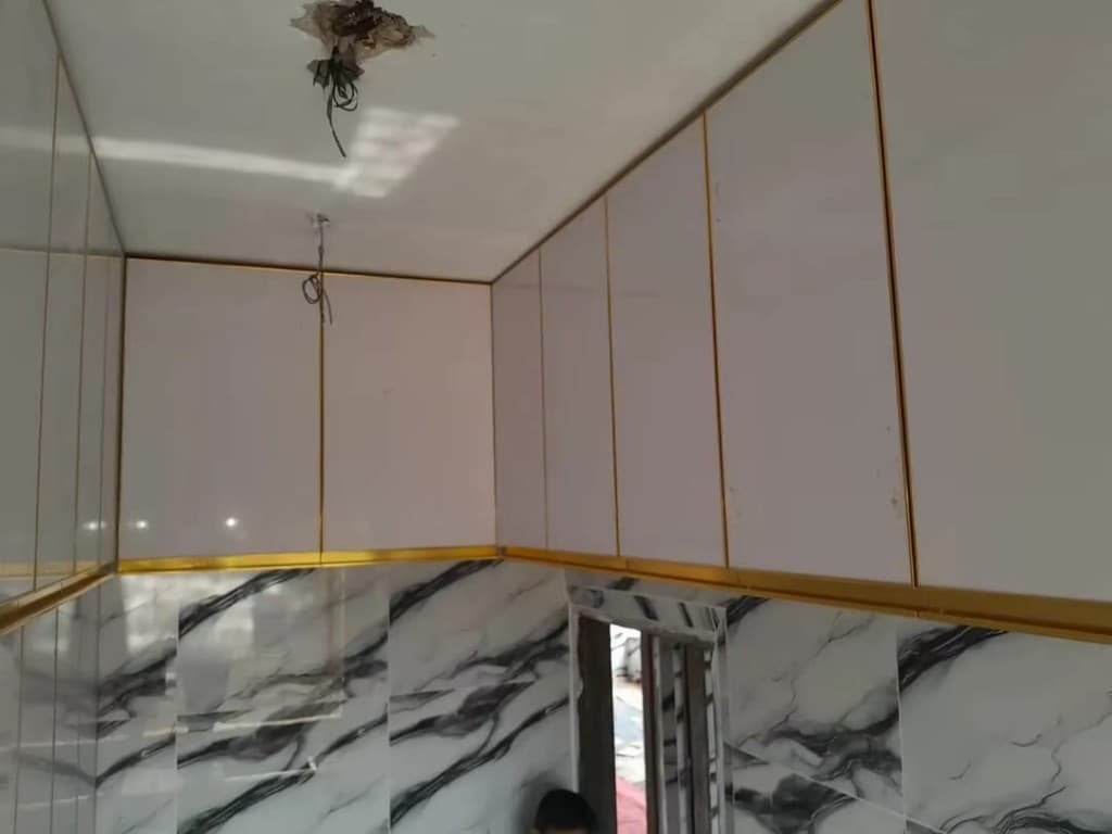 Upper kitchen cabinets with gold frames, above a marble-clad wall.